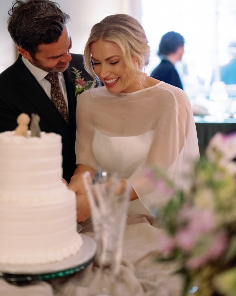 Bride and groom smile together beside their wedding cake during their intimate garden party reception in Charlotte.