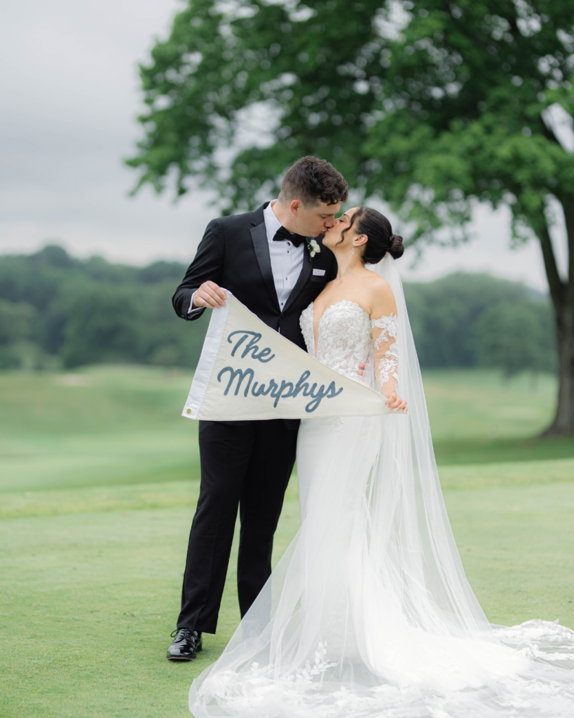 Photo of bride and groom on golf course holding pennant with last name
