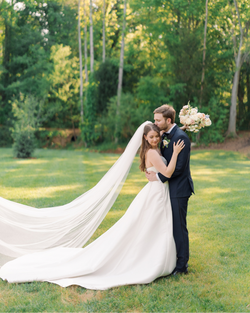 Emma and Cameron embrace during outdoor wedding portraits on the green grounds of Splendor Pond in Mooresville, North Carolina.