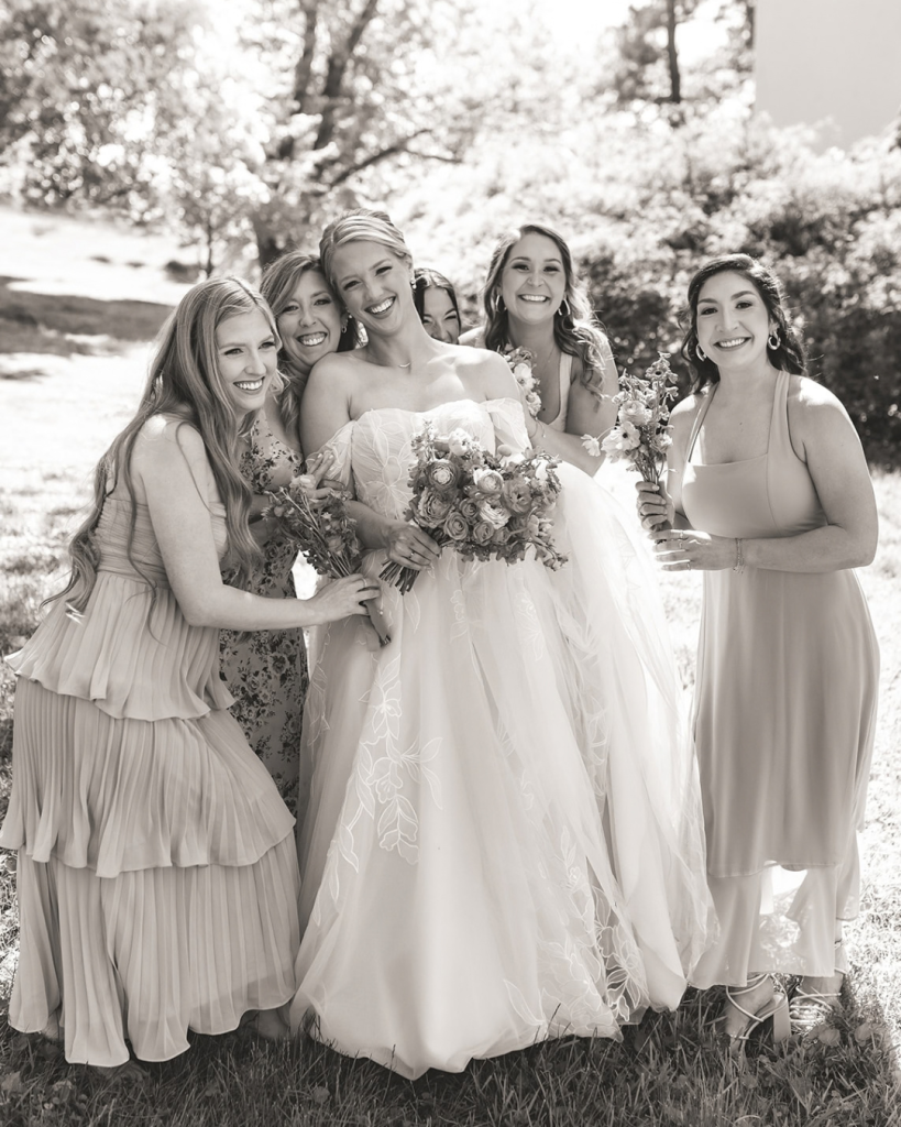 bride and brides maids smiling while bride holds bouquet