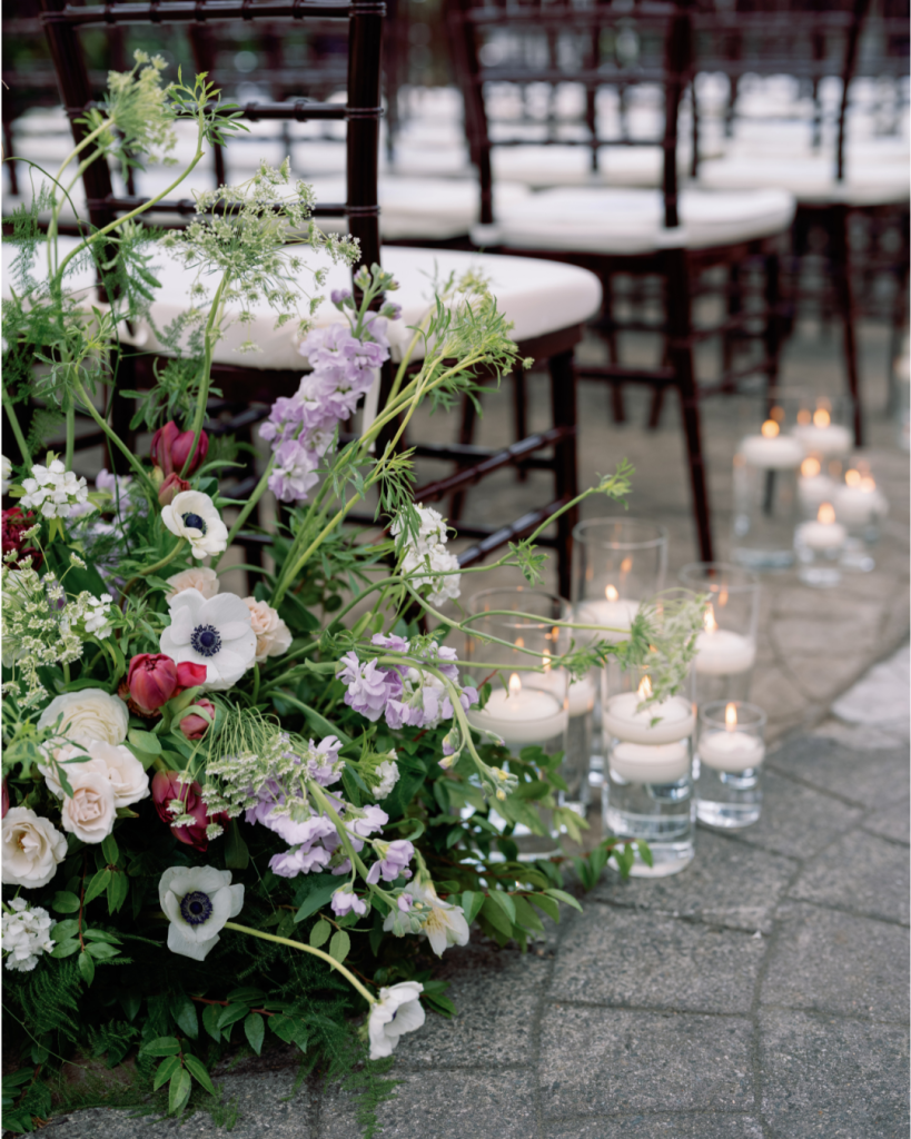 Romantic garden wedding ceremony florals featuring white anemones, pink blooms, lavender flowers, greenery, and glowing candles.
