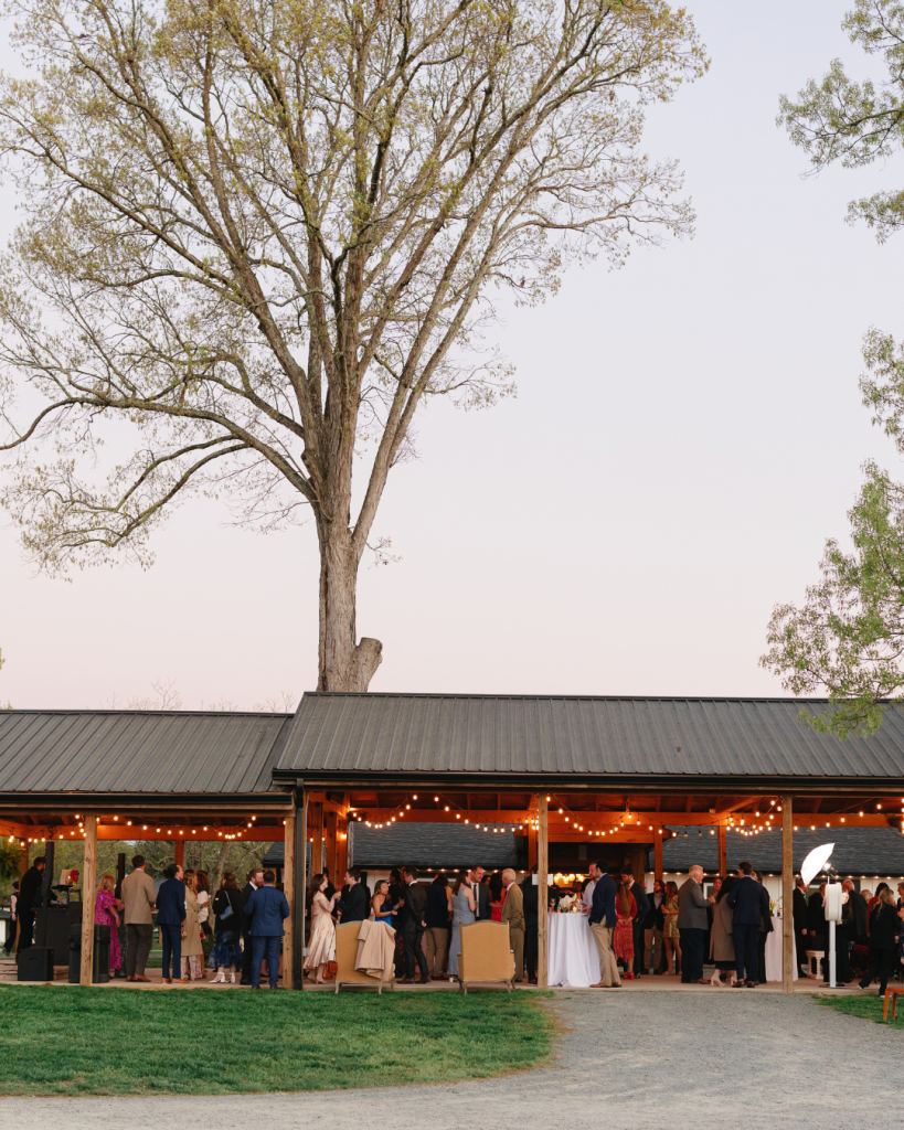 Guests gather beneath string lights in the open air pavilion during Tate and Alex’s wedding reception in Monroe, North Carolina.