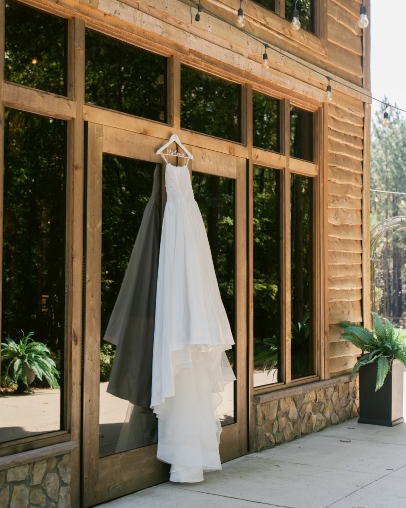 Abby's strapless white wedding gown hangs from a wooden doorway at Cedar Hills, surrounded by rustic wood siding and large windows.