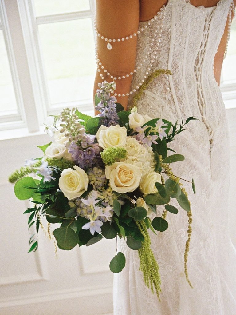 Bride holding a white and purple bridal bouquet in front of her wedding dress.