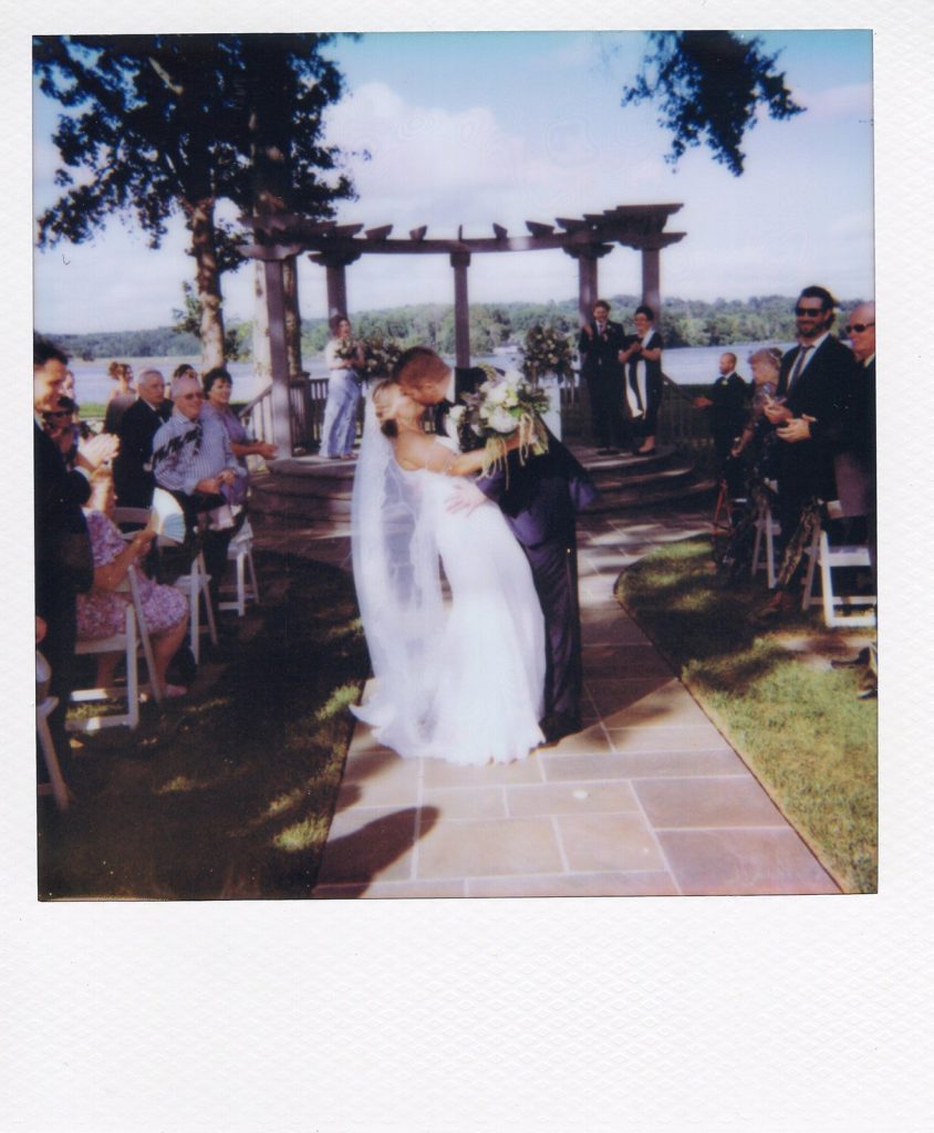 Bride in a white gown and groom in a navy blue tuxedo dipping and kissing his bride during the ceremony