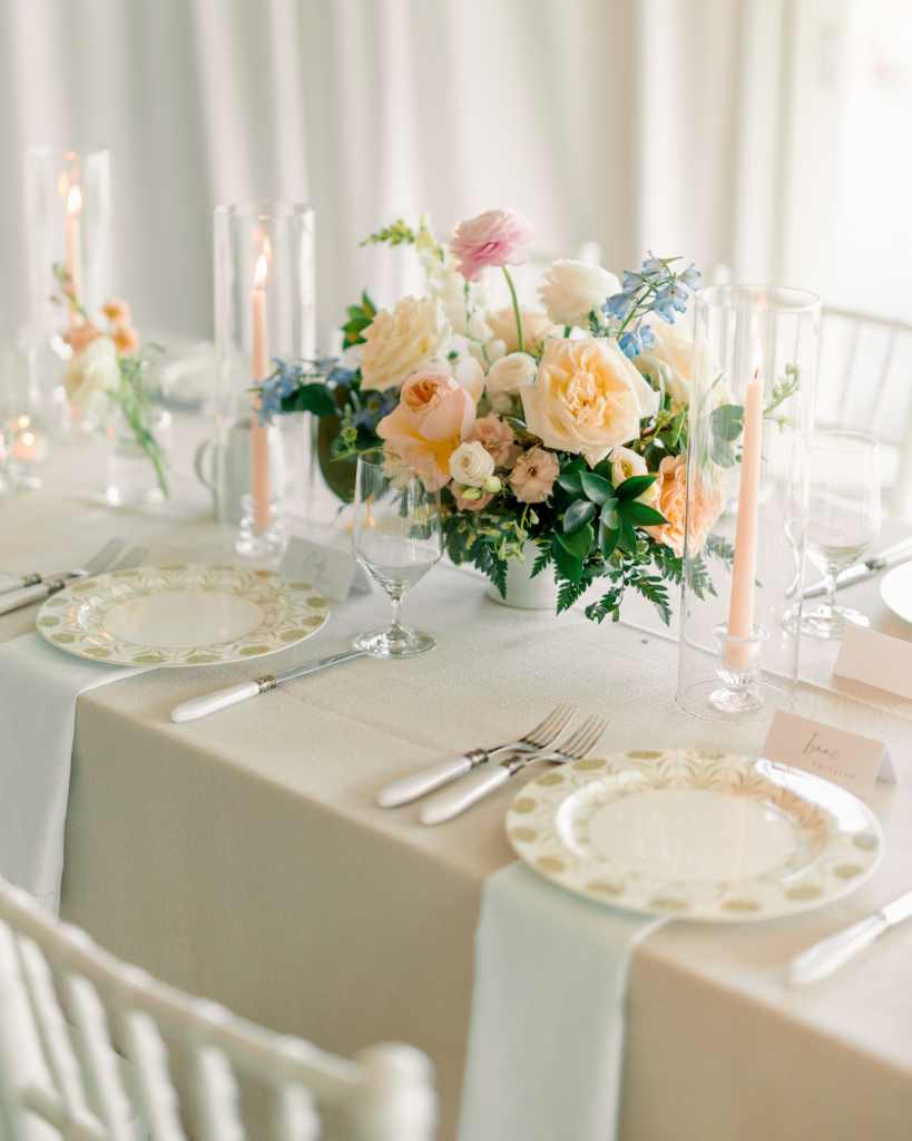 Romantic wedding reception table styled with peach taper candles, spring floral centerpieces and patterned place settings.