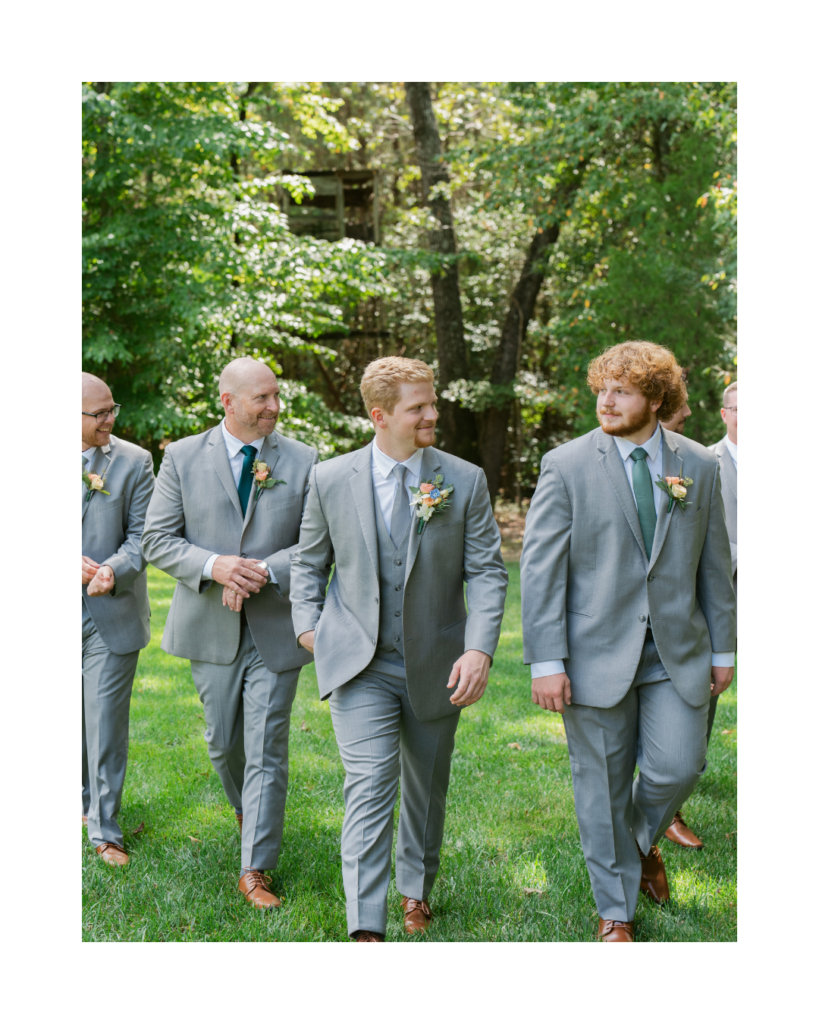 Connor walks outdoors with his groomsmen in coordinated light gray suits, blue and green ties, and colorful floral boutonnieres.