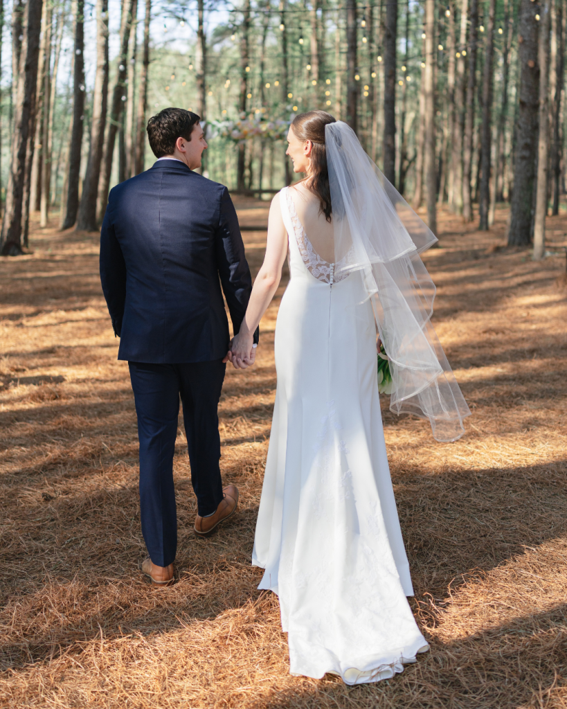 Tate and Alex walk hand in hand through the pine trees during wedding portraits at The Union Exchange.