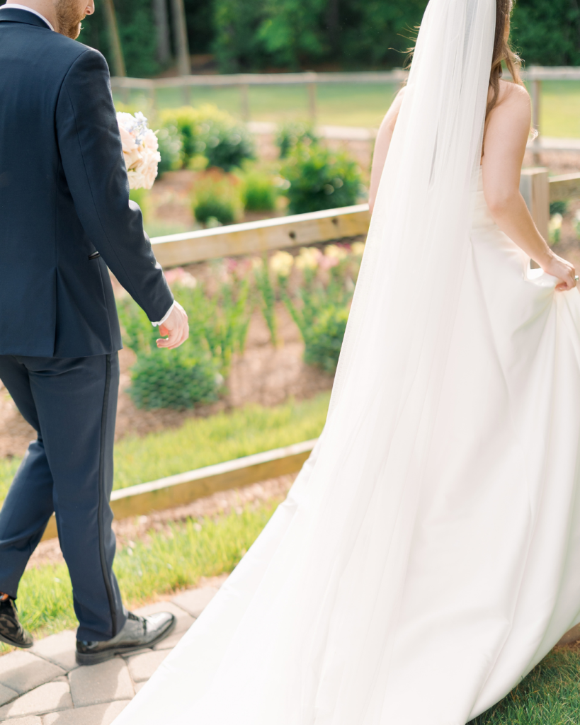 Emma and Cameron walk together after their ceremony with Emma’s long white veil and wedding gown flowing behind her.