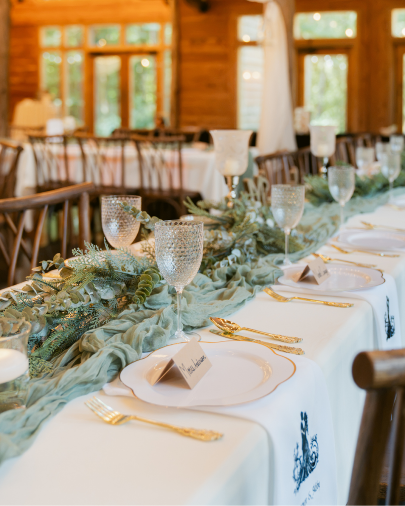 Wedding reception tablescape at Cedar Hills featuring soft green fabric runners, textured glass goblets, gold flatware, and natural greenery.