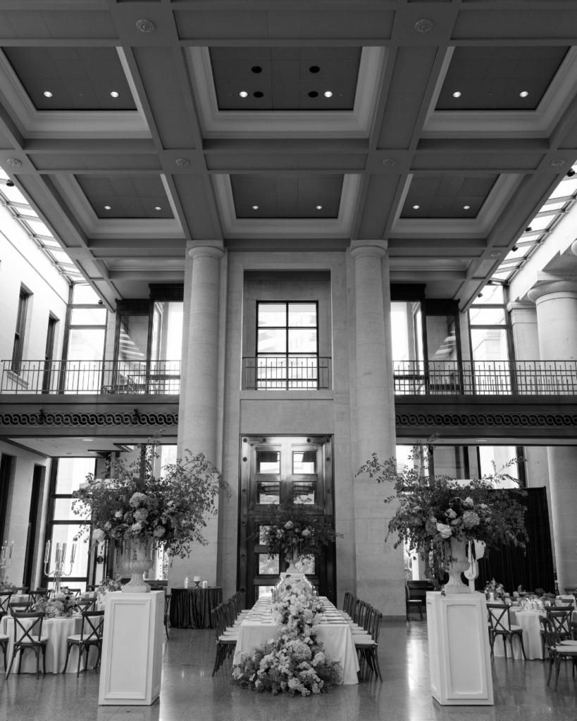 Grand Ohio Statehouse wedding reception with towering stone columns, lush floral urns, a long head table and a black-and-white checkered dance floor.