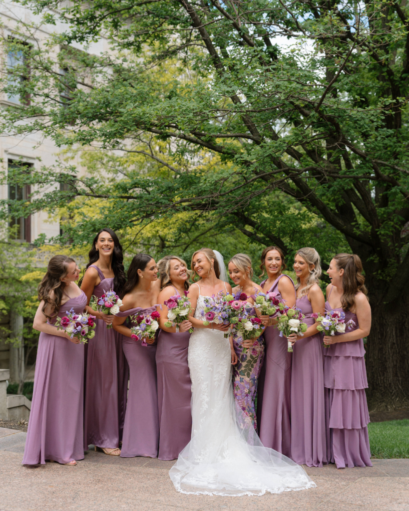 Bride Chelsea poses with bridesmaids in mauve and lavender dresses holding colorful spring wedding bouquets in Columbus, Ohio.