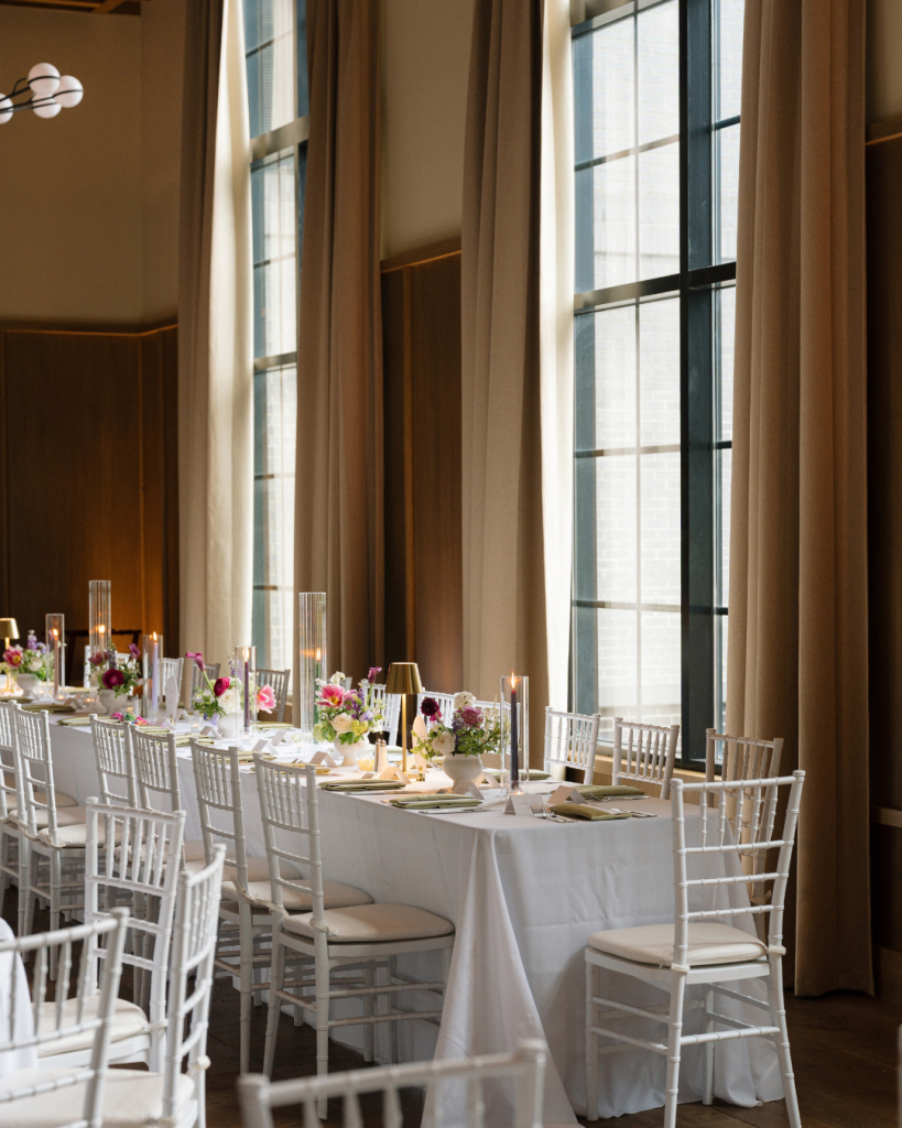 Elegant wedding reception at The Junto featuring long white tables, colorful floral arrangements, olive green napkins, and candlelight.