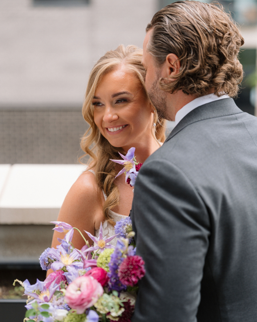 Intimate wedding portrait of Chelsea smiling as Matt kisses her forehead, surrounded by vibrant spring bridal flowers.
