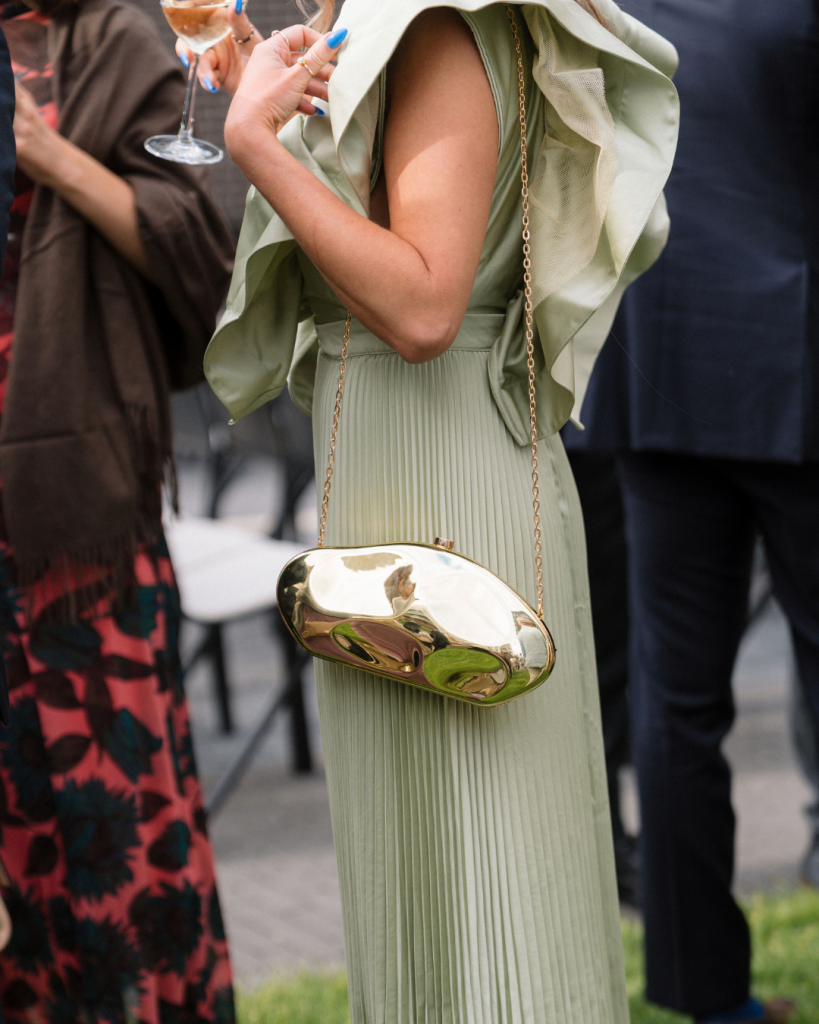 Wedding guest wearing a sage green pleated dress and carrying a metallic gold clutch at Chelsea and Matt's Columbus wedding.