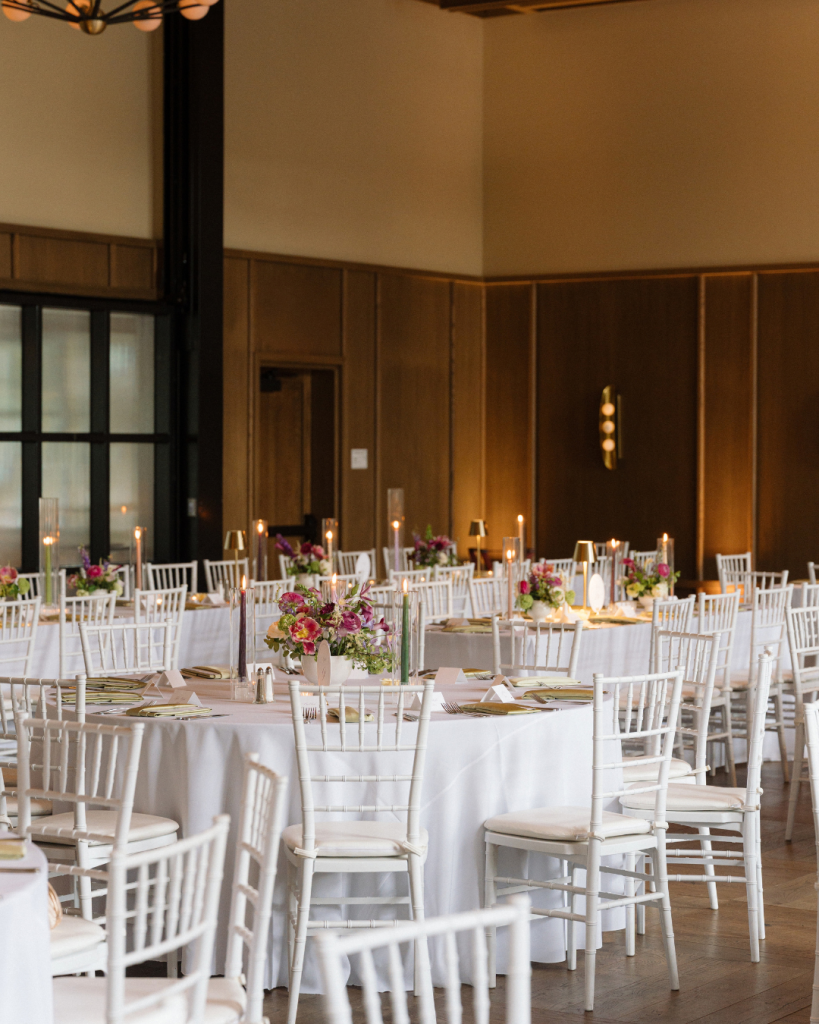 Romantic indoor wedding reception with colorful spring centerpieces, white chairs, and glowing candles at The Junto in Columbus.