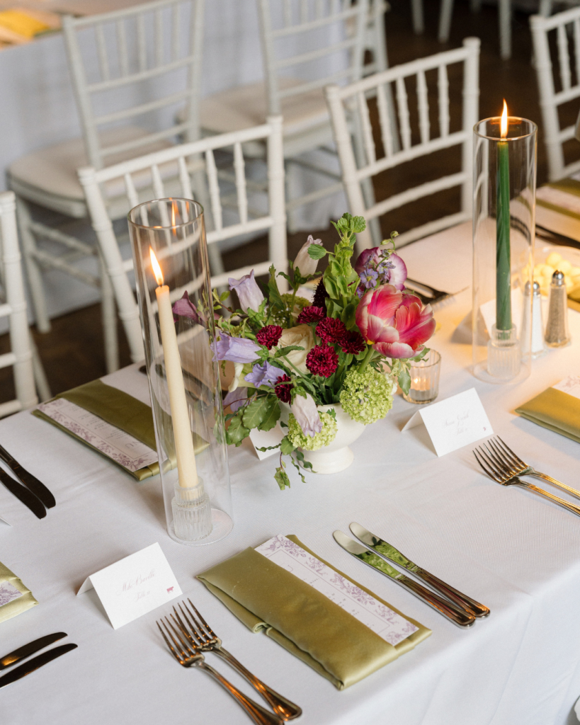 Colorful spring wedding centerpiece with purple and pink flowers, olive green napkins, and taper candles at The Junto in Columbus