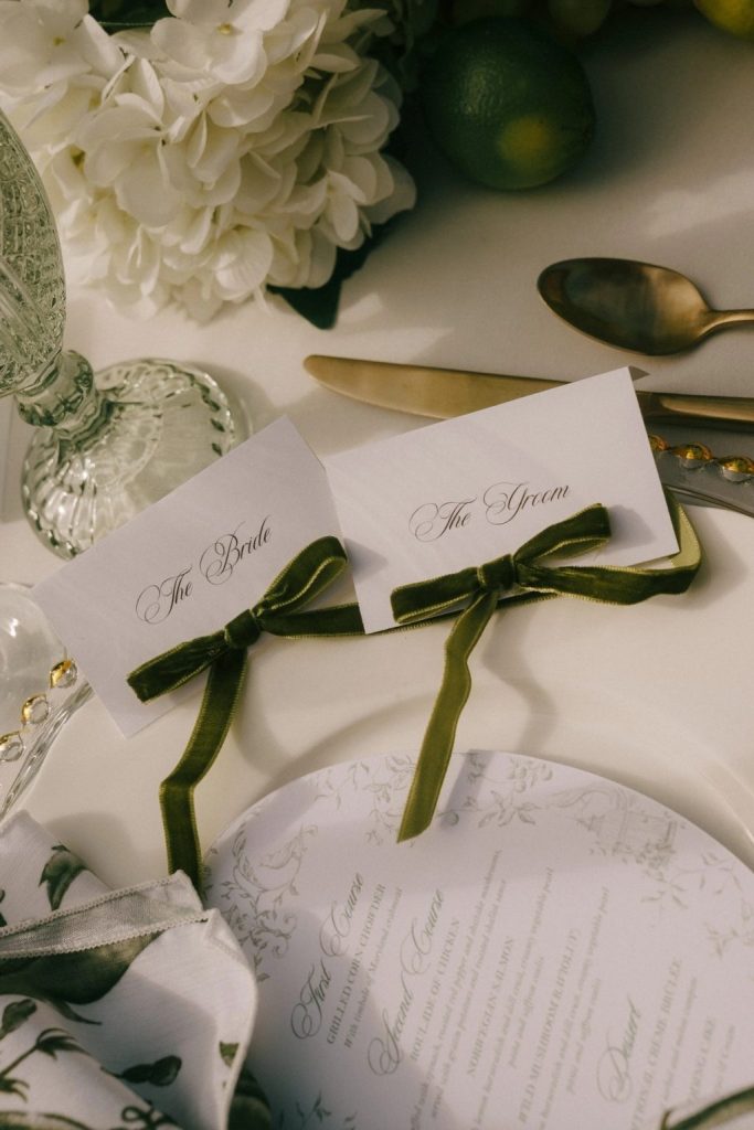 Elegant wedding place cards with olive green velvet bows, ivory hydrangeas, gold flatware, and personalized stationery inspiring Columbus wedding favors and details.
