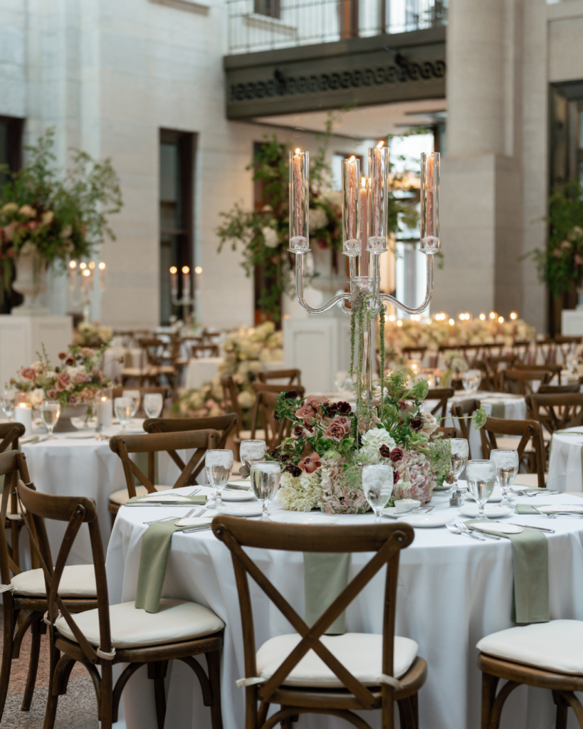 Romantic Ohio Statehouse wedding reception table featuring blush and burgundy floral centerpieces, tall glass candelabras, sage green napkins and wooden chairs.