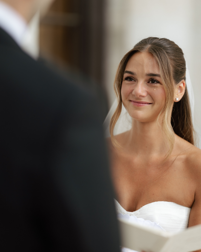 Emotional bride Hannah smiles through tears while looking at groom Ben during their wedding ceremony in Columbus, Ohio.