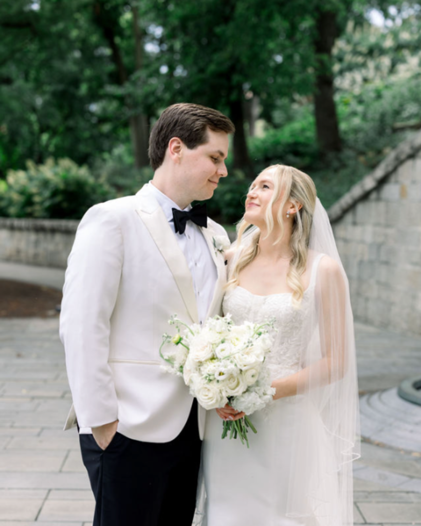 Elizabeth and Carter pose outdoors on their Columbus wedding day, with a white bridal bouquet and an ivory dinner jacket.