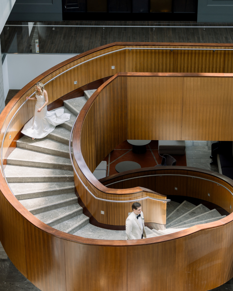 Elizabeth descends a curved wooden staircase with Carter below during their wedding portraits in Columbus, Ohio.