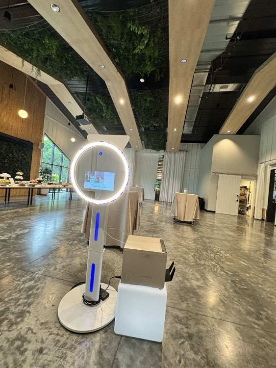 Event Captura's modern 360-style photo booth setup with a circular LED light, touchscreen display, and white equipment at an elegant indoor event venue.