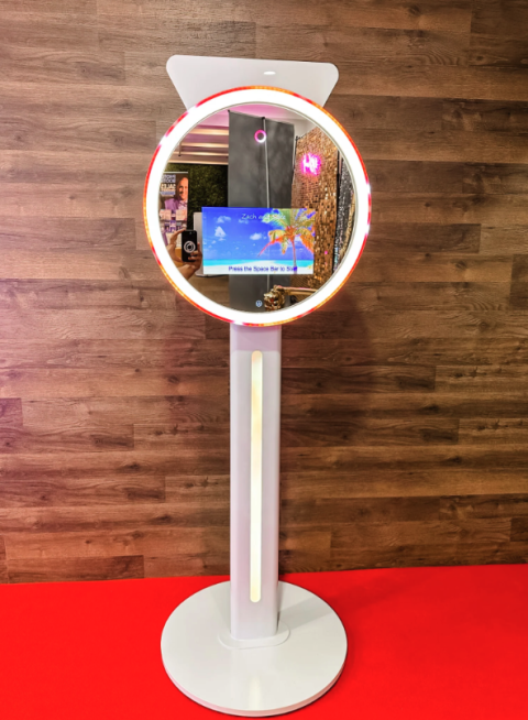 Event Captura's sleek white digital photo booth featuring a circular LED light, interactive touchscreen, and modern freestanding design against a wooden wall.
