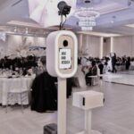Event Captura's white wedding photo booth setup featuring professional umbrella lighting, a personalized Javi and Jessica display, and a printer inside an elegant ballroom reception.
