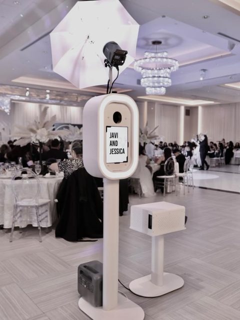 Event Captura's white wedding photo booth setup featuring professional umbrella lighting, a personalized Javi and Jessica display, and a printer inside an elegant ballroom reception.