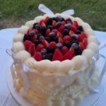 Helu Sweets Bakery custom vintage-style cake featuring intricate ivory buttercream piping, delicate white ribbon bows, and fresh strawberries, raspberries, blueberries, and blackberries.
