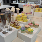 Helu Sweets Bakery dessert table featuring individual strawberry cheesecake cups, chocolate dessert parfaits, miniature cupcakes, cake pops, and elegant red and white floral arrangements.