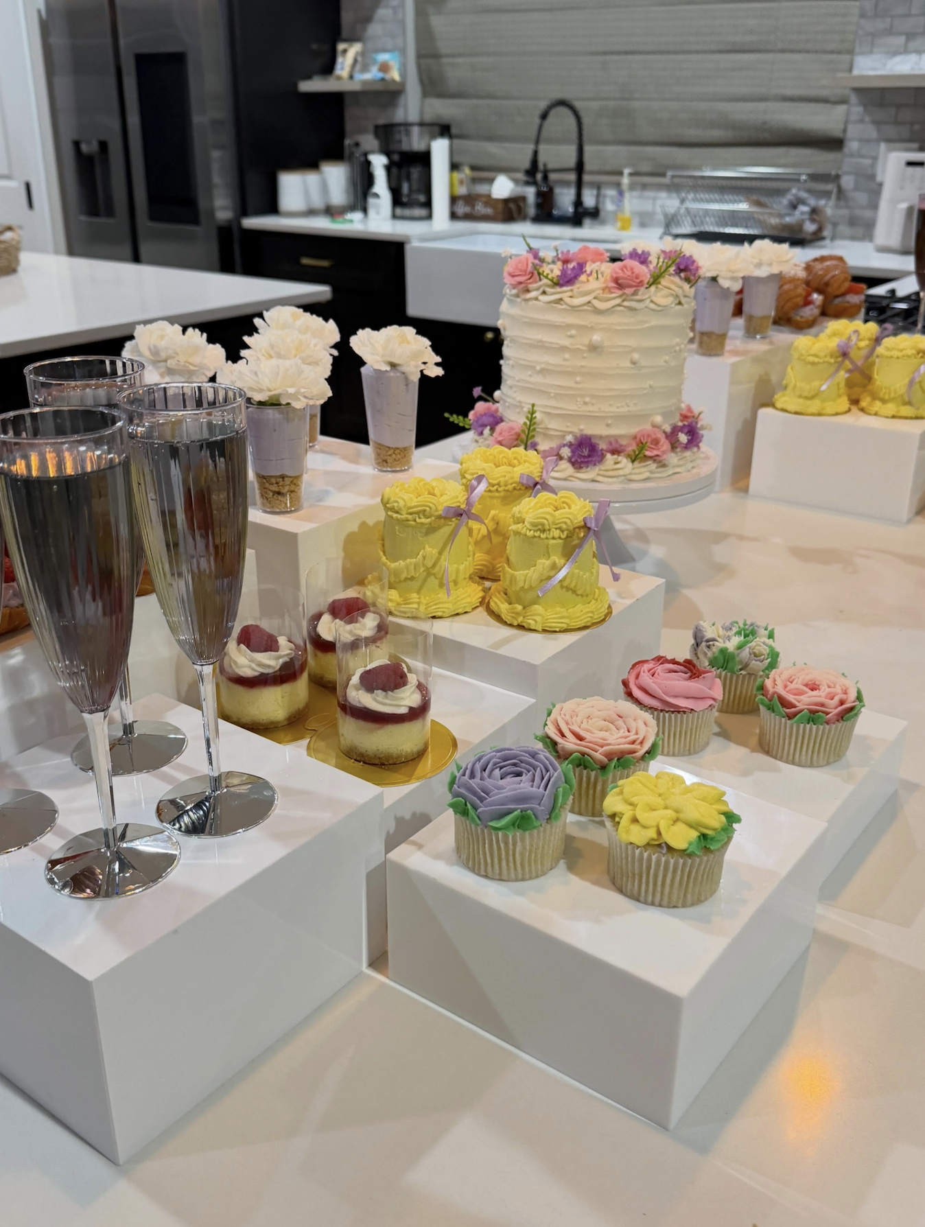 Helu Sweets Bakery dessert table featuring individual strawberry cheesecake cups, chocolate dessert parfaits, miniature cupcakes, cake pops, and elegant red and white floral arrangements.