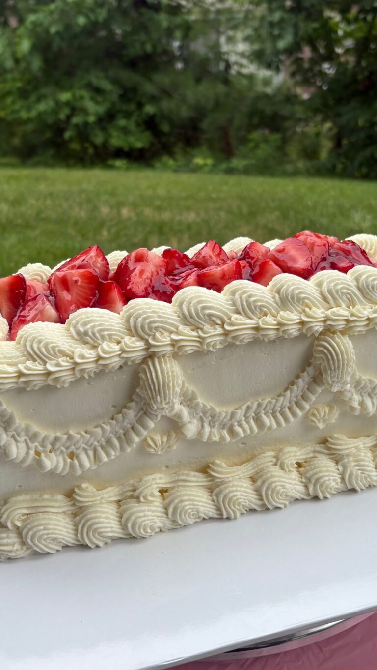 Helu Sweets Bakery rectangular vintage-inspired cake featuring elaborate ivory buttercream piping, decorative frosting swags, and fresh glazed strawberries displayed outdoors.