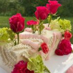 Helu Sweets Bakery romantic rectangular cake featuring delicate ivory and blush pink buttercream piping, vibrant pink roses, pink carnations, and soft green floral accents.