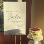 Helu Sweets Bakery custom vintage-style berry cake displayed beside a personalized bridal celebration sign featuring delicate ivory buttercream piping, white ribbon bows, and fresh mixed berries.
