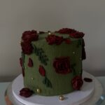 Helu Sweets Bakery custom dark green cake featuring textured buttercream frosting, deep burgundy buttercream roses, delicate green leaves, and elegant gold pearl accents.