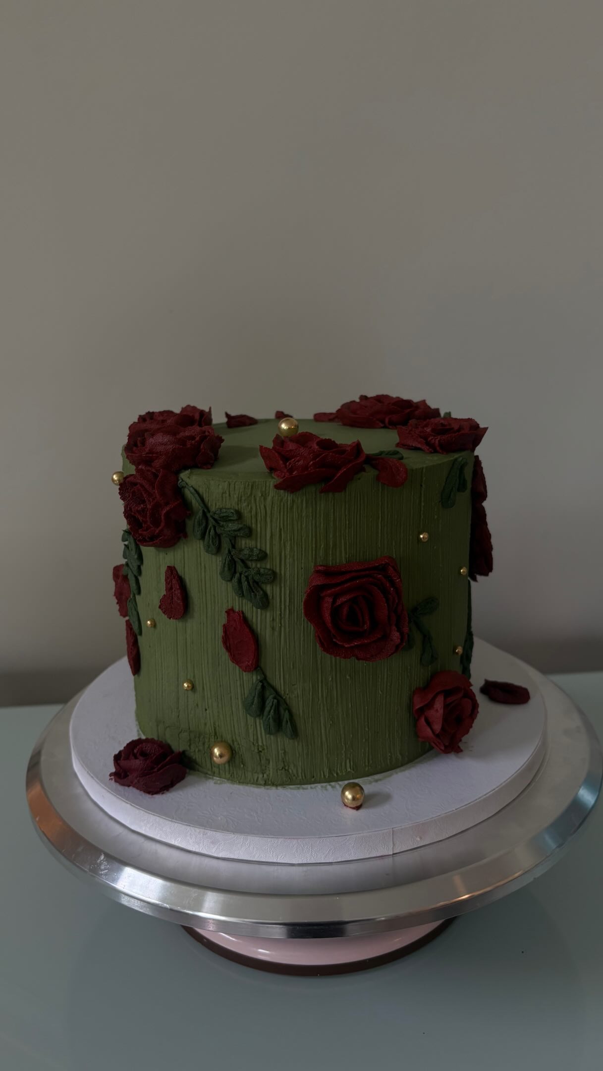 Helu Sweets Bakery custom dark green cake featuring textured buttercream frosting, deep burgundy buttercream roses, delicate green leaves, and elegant gold pearl accents.