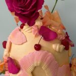 Helu Sweets Bakery artistic buttercream cake decorated with sculptural pink and ivory frosting, vibrant magenta roses, peach-colored floral accents, fresh cherries, and raspberries.