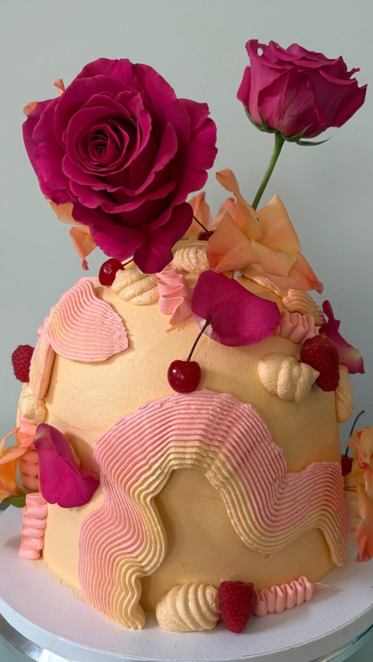 Helu Sweets Bakery artistic buttercream cake decorated with sculptural pink and ivory frosting, vibrant magenta roses, peach-colored floral accents, fresh cherries, and raspberries.
