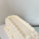Helu Sweets Bakery elegant rectangular white cake featuring smooth ivory buttercream frosting and intricate vintage-style piped borders and decorative swags.