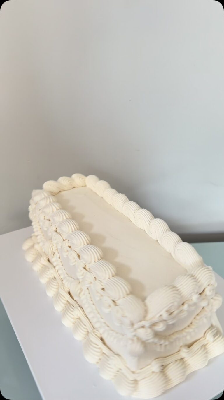Helu Sweets Bakery elegant rectangular white cake featuring smooth ivory buttercream frosting and intricate vintage-style piped borders and decorative swags.
