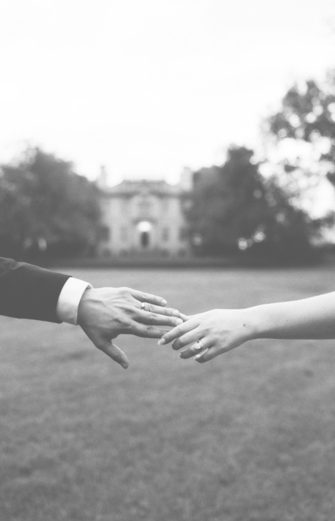 Bride and groom holding hands outdoors with a historic stone estate in the background.
