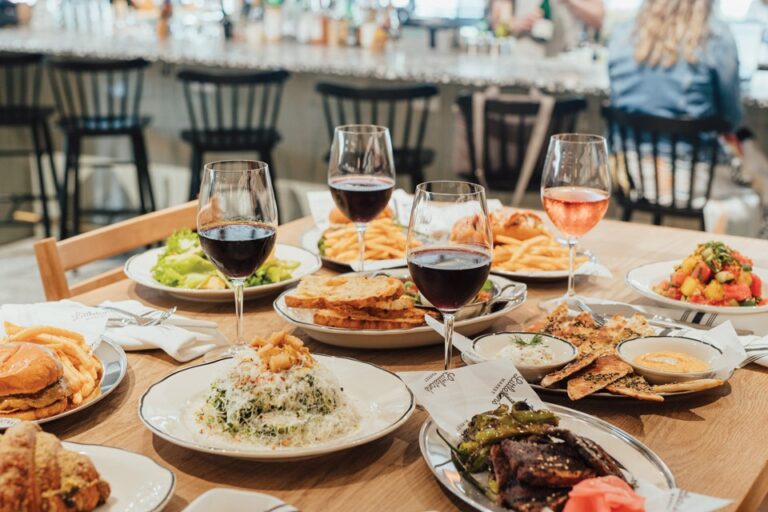 Table filled with gourmet entrées, fresh salads, sandwiches, fries, and glasses of red and rosé wine at Littleton’s Market in Upper Arlington.
