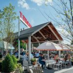 Outdoor patio dining area at Littleton’s Market in Upper Arlington, Ohio, featuring shaded tables, white umbrellas, greenery, and guests enjoying the sunny weather.