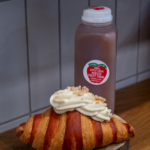 Flaky golden croissant topped with whipped cream beside a bottle of locally produced apple cider at Littleton’s Market.