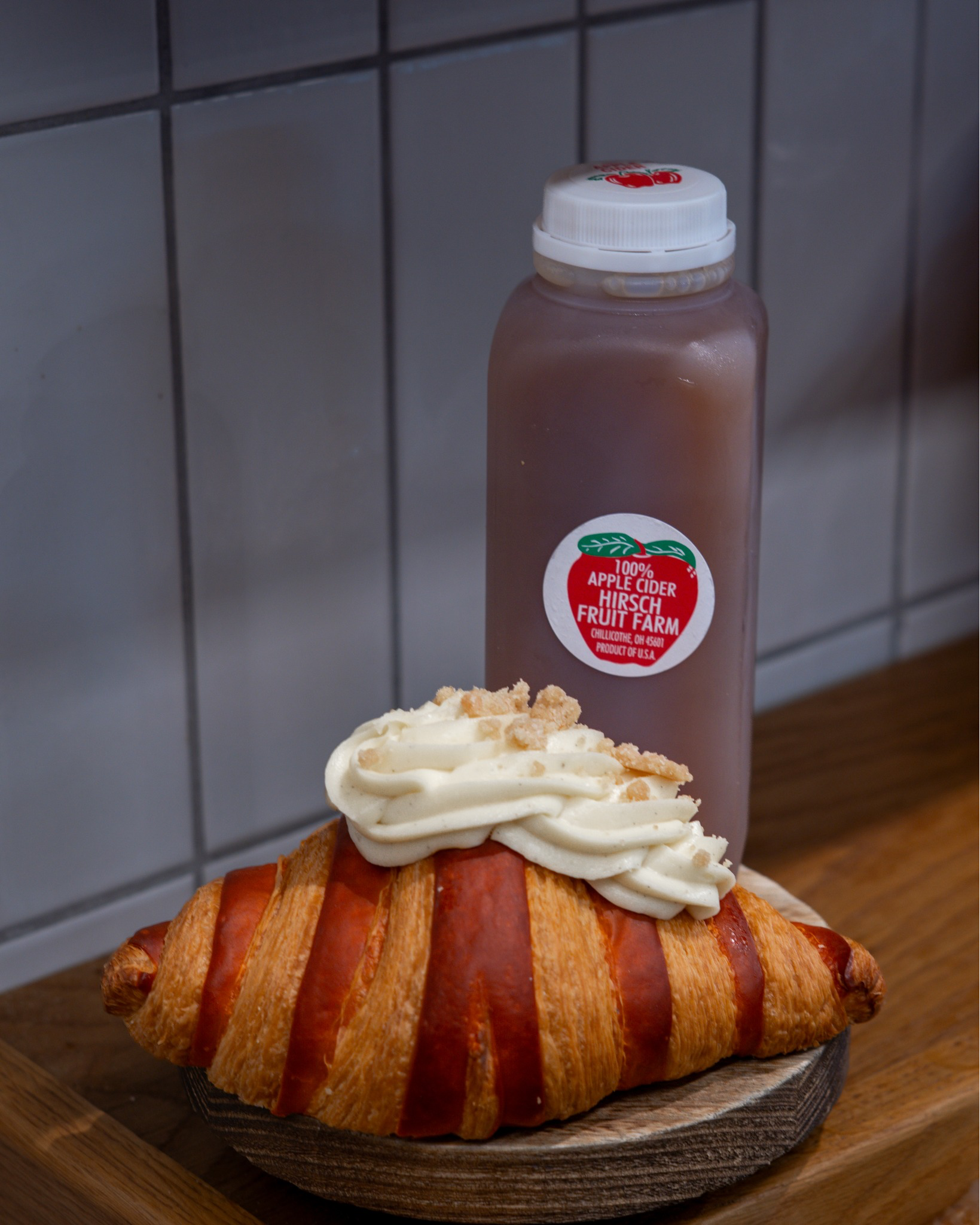 Flaky golden croissant topped with whipped cream beside a bottle of locally produced apple cider at Littleton’s Market.