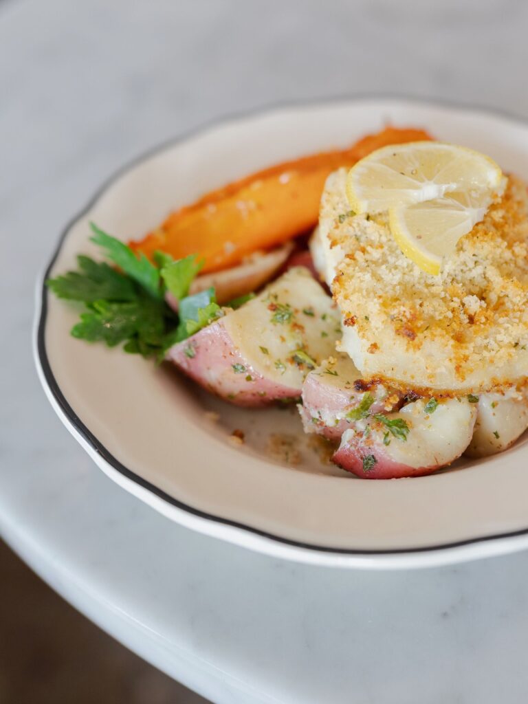 Gourmet seafood entrée featuring a golden breadcrumb crust, lemon slices, roasted potatoes, carrots, and fresh parsley at Littleton’s Market.