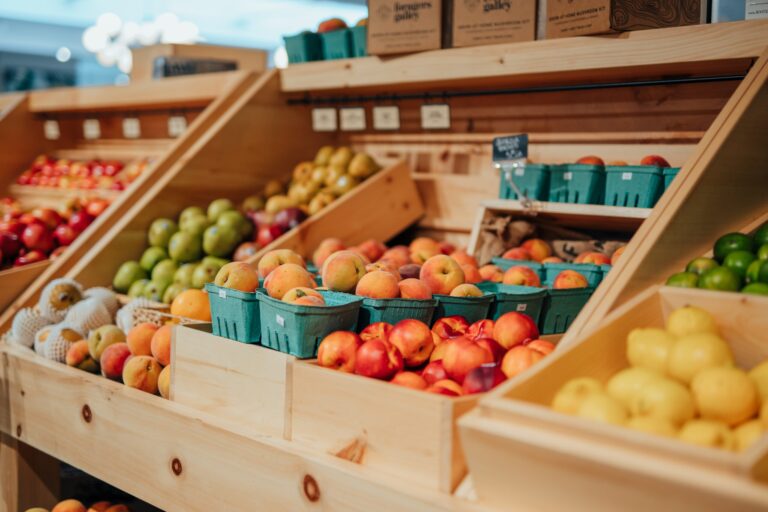 Fresh seasonal produce displayed in wooden bins at Littleton’s Market, featuring peaches, apples, pears, lemons, and other fruits.