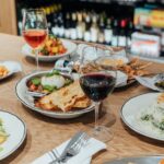 Gourmet dining spread at Littleton’s Market featuring fresh salads, burrata with toasted bread, steak, vegetables, and glasses of wine.